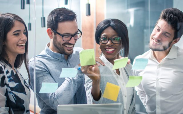 Panoramic view creative group of business people working with sticky notes on glass wall in office